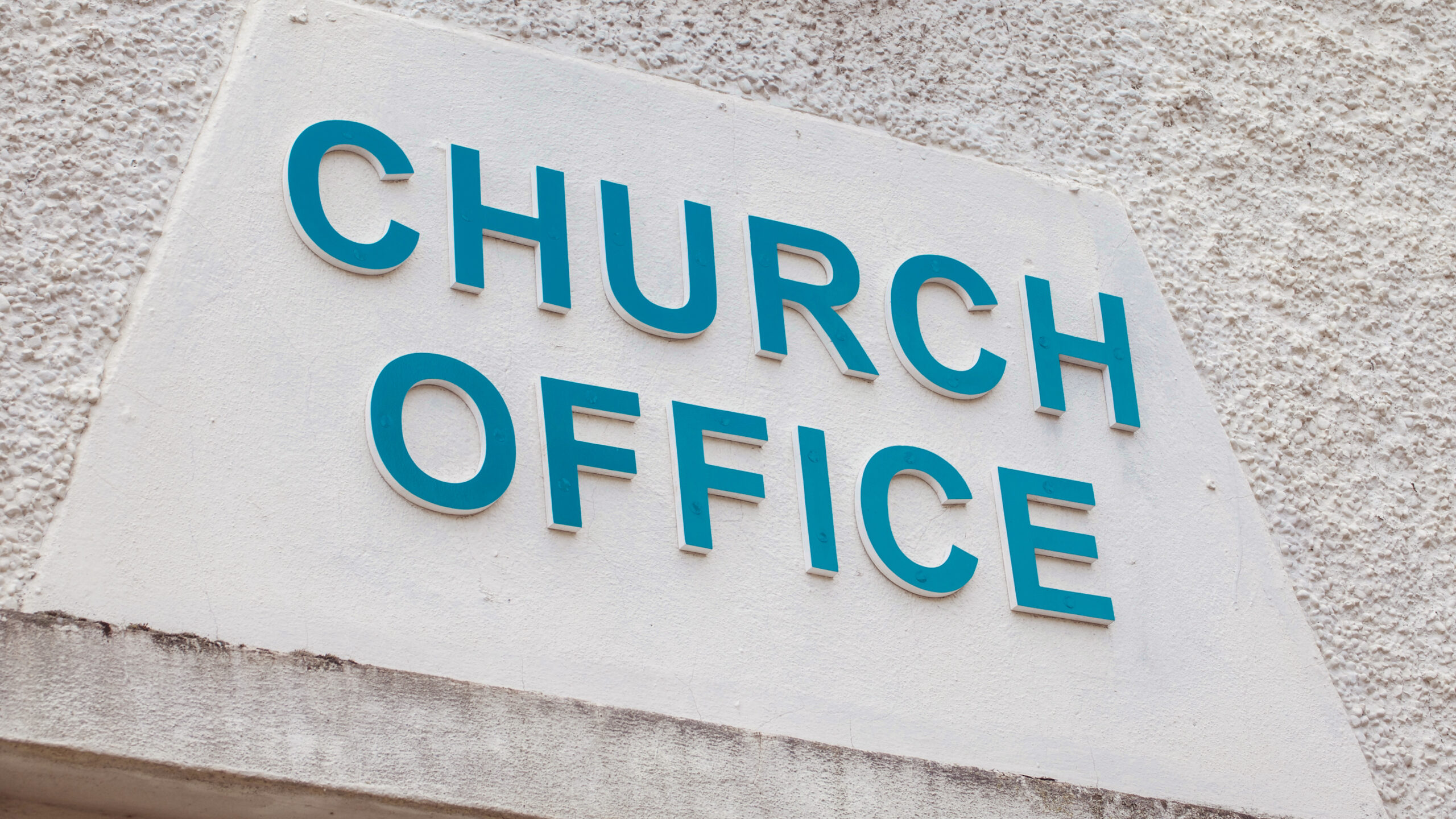 Church Office sign. Blue text on a white textured wall.