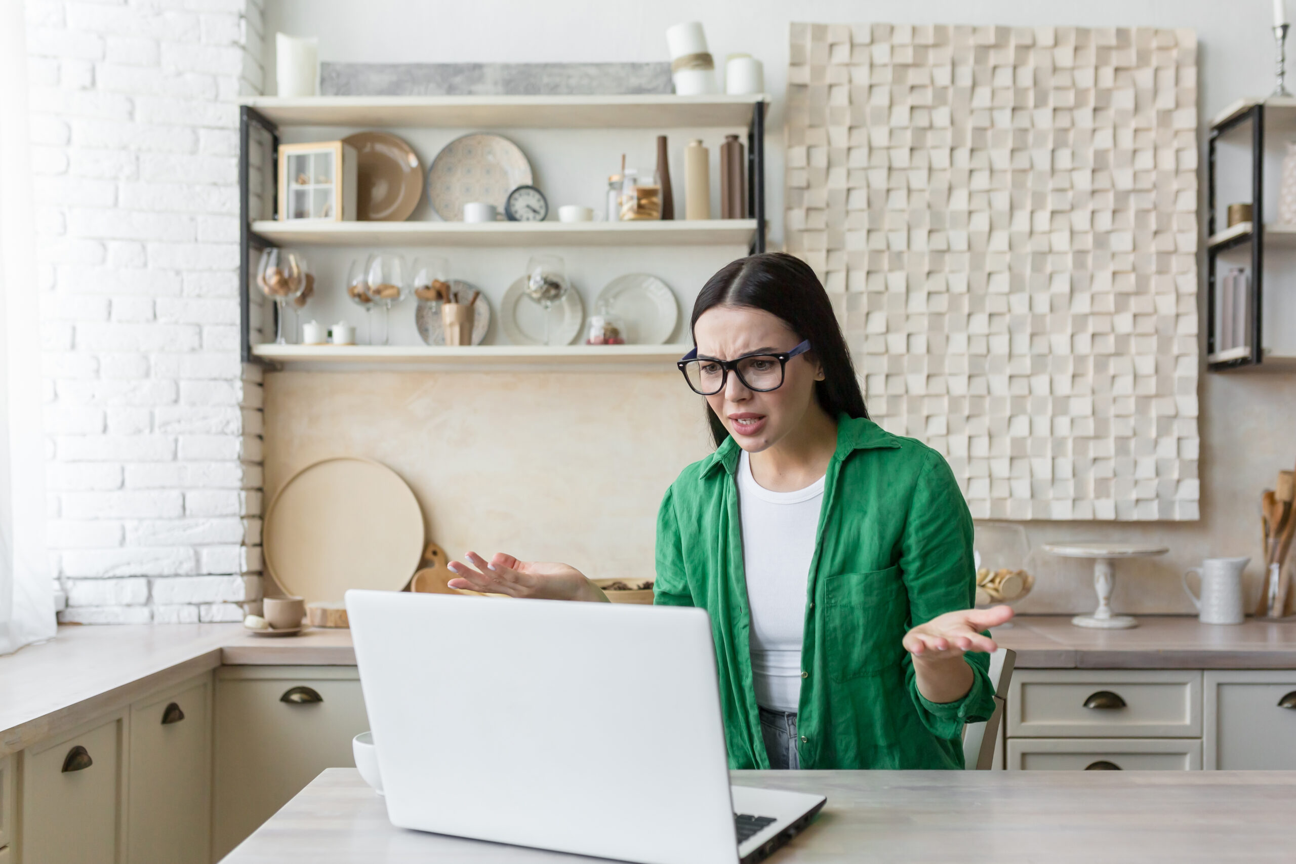 Upset young businesswoman, freelancer works from home He is sitting at the table at home, there is no Internet, the laptop is broken. He spreads his hands angrily.